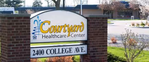 A Courtyard Healthcare Center sign with brick columns near a parking lot.