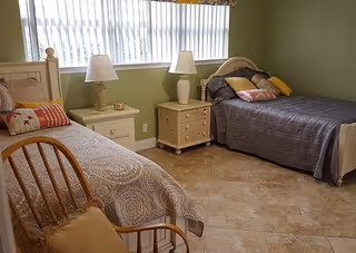 Two twin beds in a shared bedroom with nightstands, lamps, and a wooden chair.