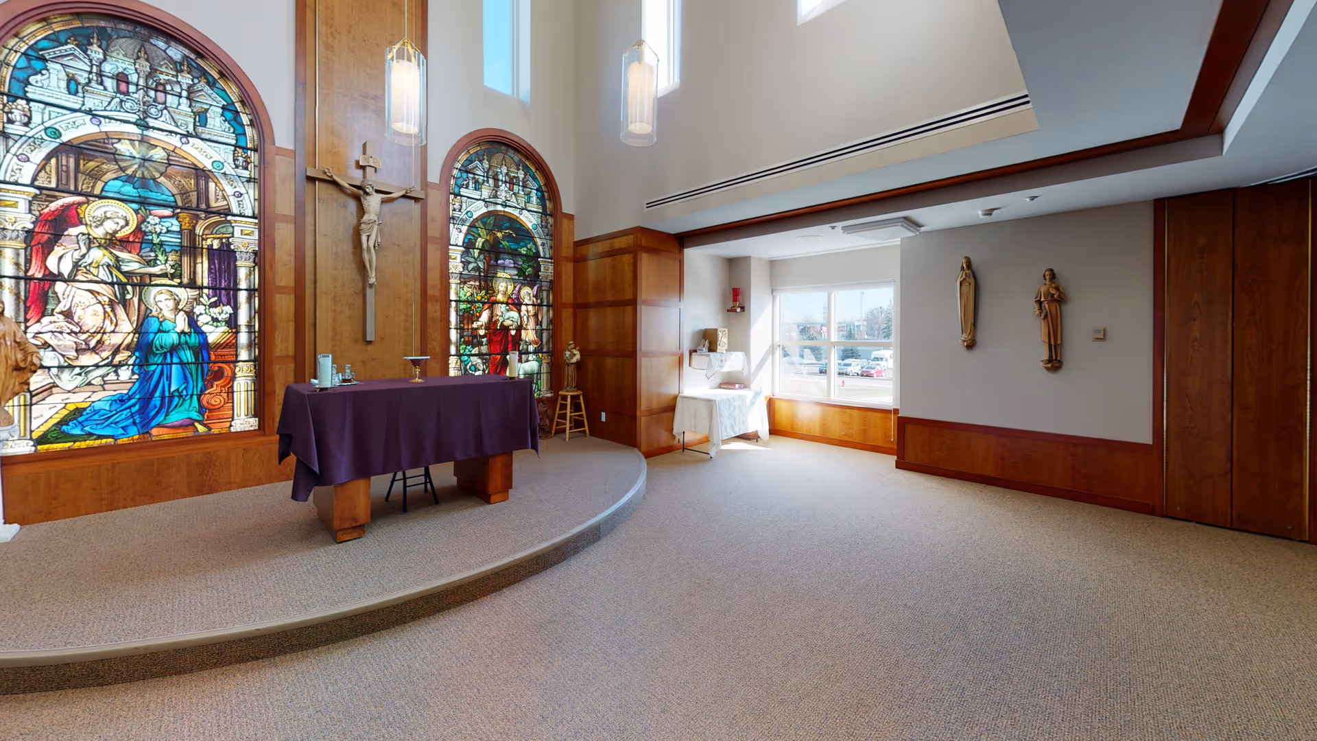 Church-like chapel interior featuring stained-glass windows, a crucifix, altar, and wooden paneling.