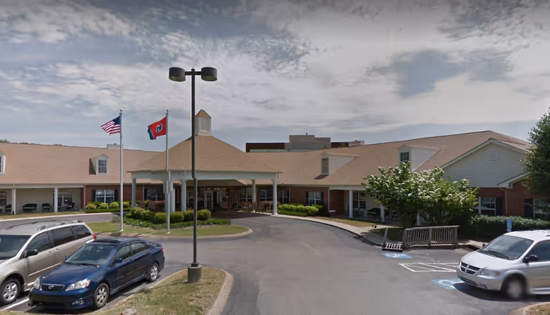 Exterior view of Southerland Place senior living facility with flags and parked cars.