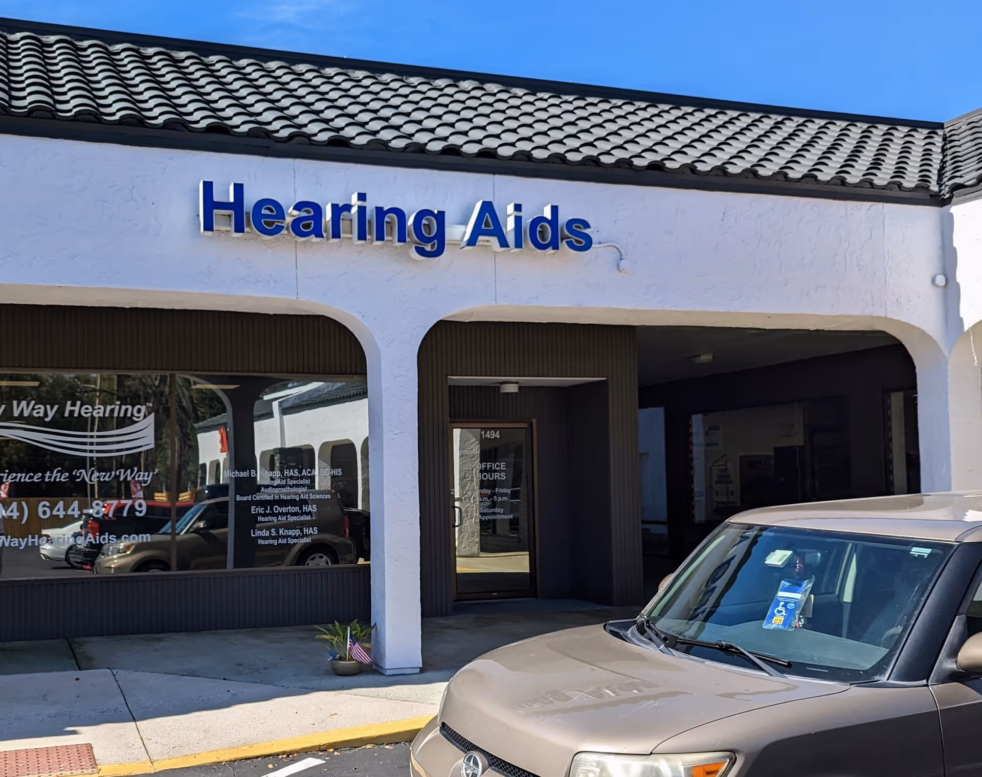 White storefront with blue 'Hearing Aids' sign and a parked SUV in front
