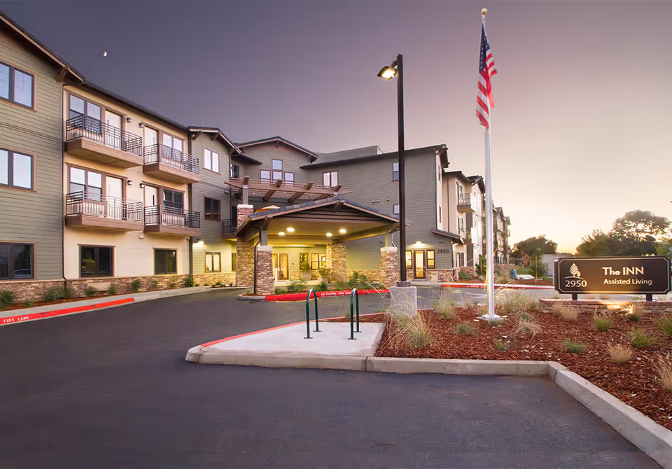 Exterior view of an assisted living facility entrance with sign, flagpole, and drive-up entry.