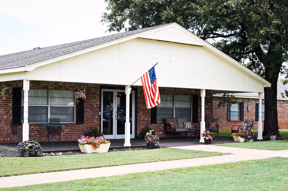 Exterior view of Meridian Nursing Home with front porch seating and an American flag.