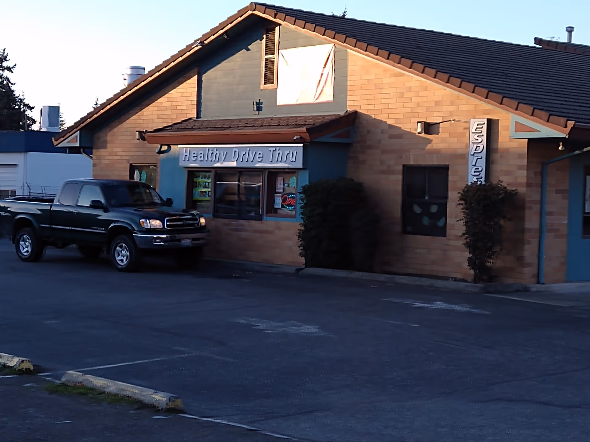 Exterior view of a brick building with 'Healthy Drive Thru' sign and a parked pickup.