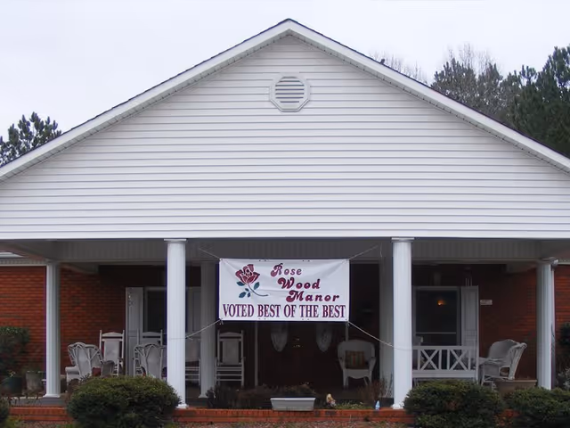 White building front with a porch and Rose Wood Manor banner