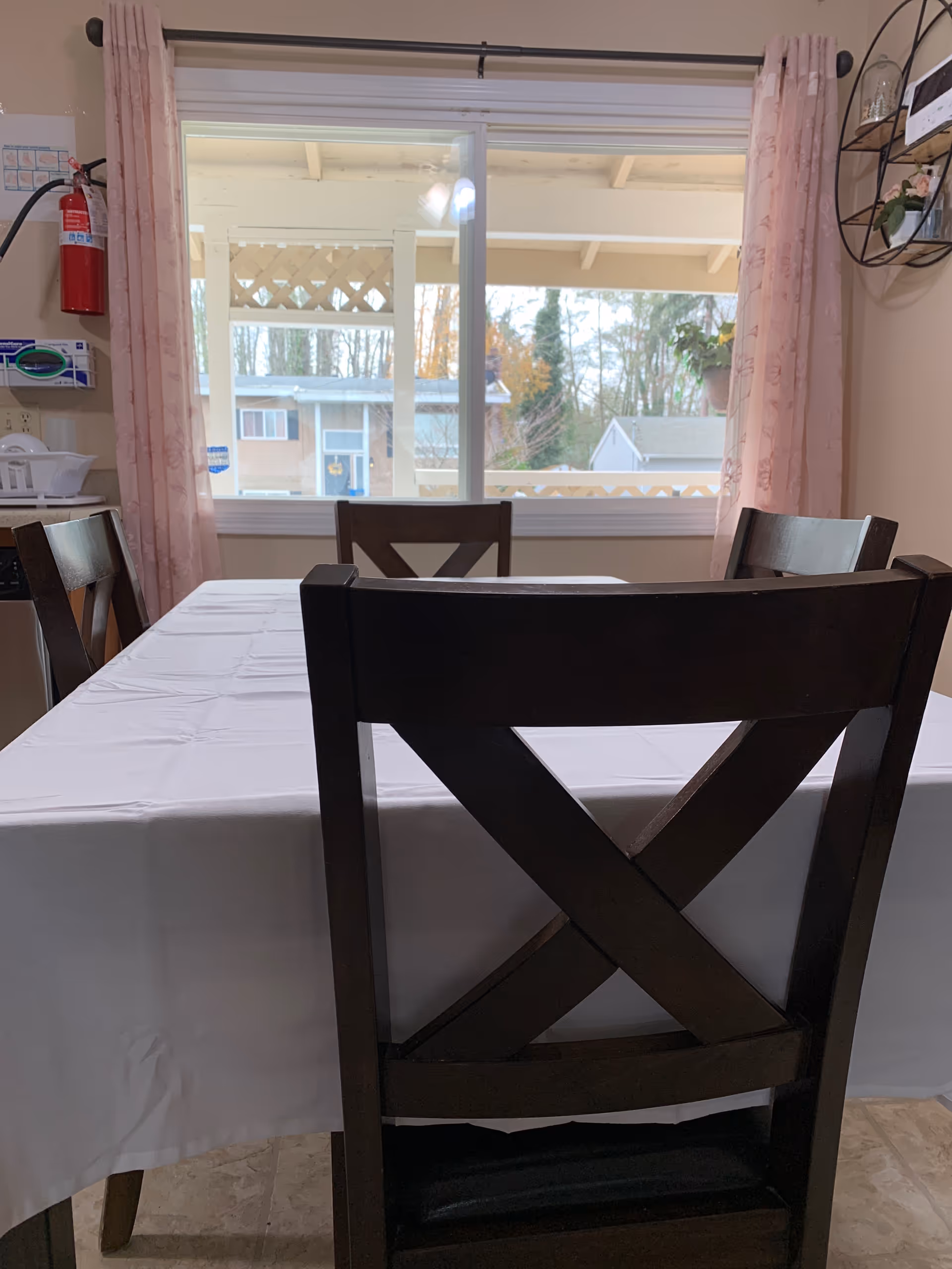 Dining table with white cloth and dark wooden chairs by a large window.