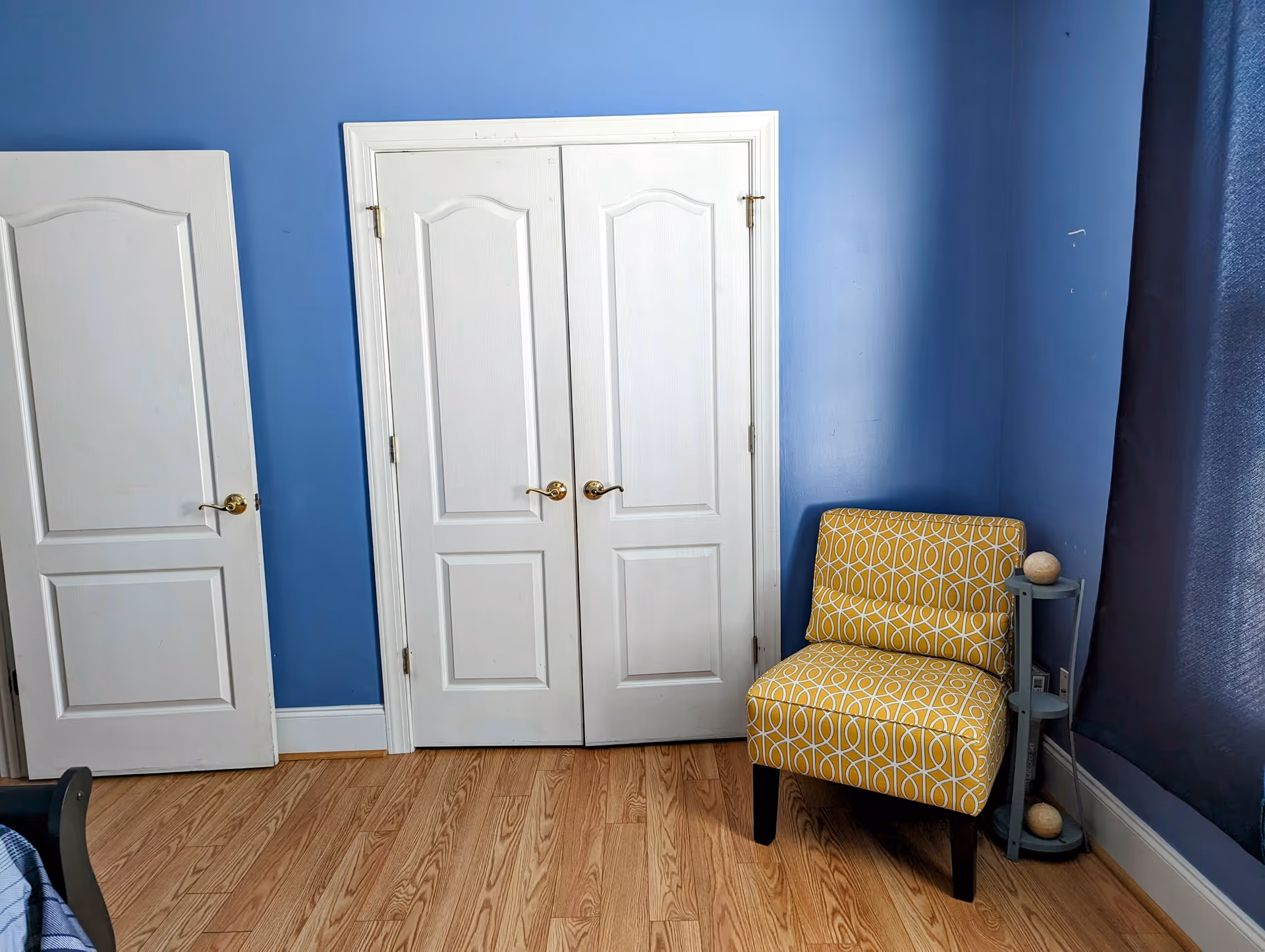 Blue walls, white double doors, and a yellow patterned chair in a cozy room.