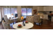 Cozy communal dining area with round tables, patterned chairs, and a visible kitchen in the back.