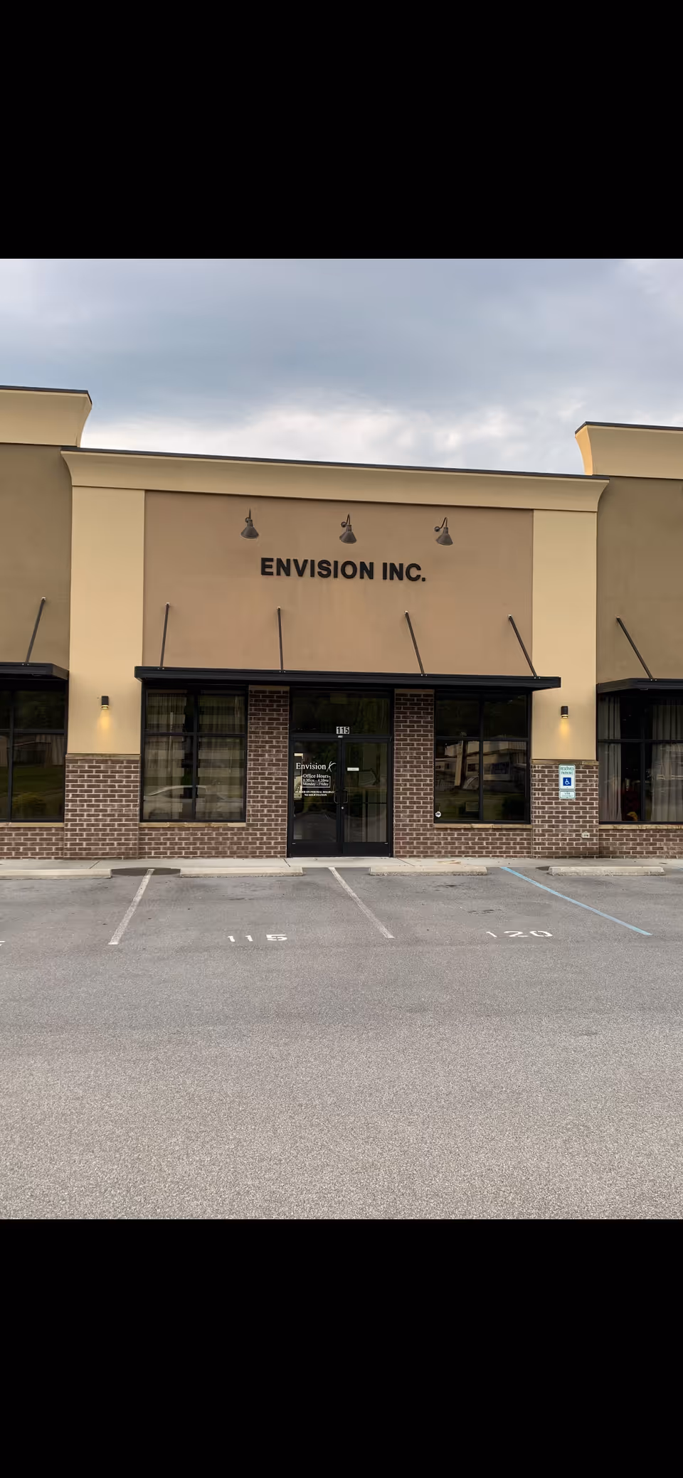 Front view of Envision Inc. storefront entrance with beige facade and brick accents.