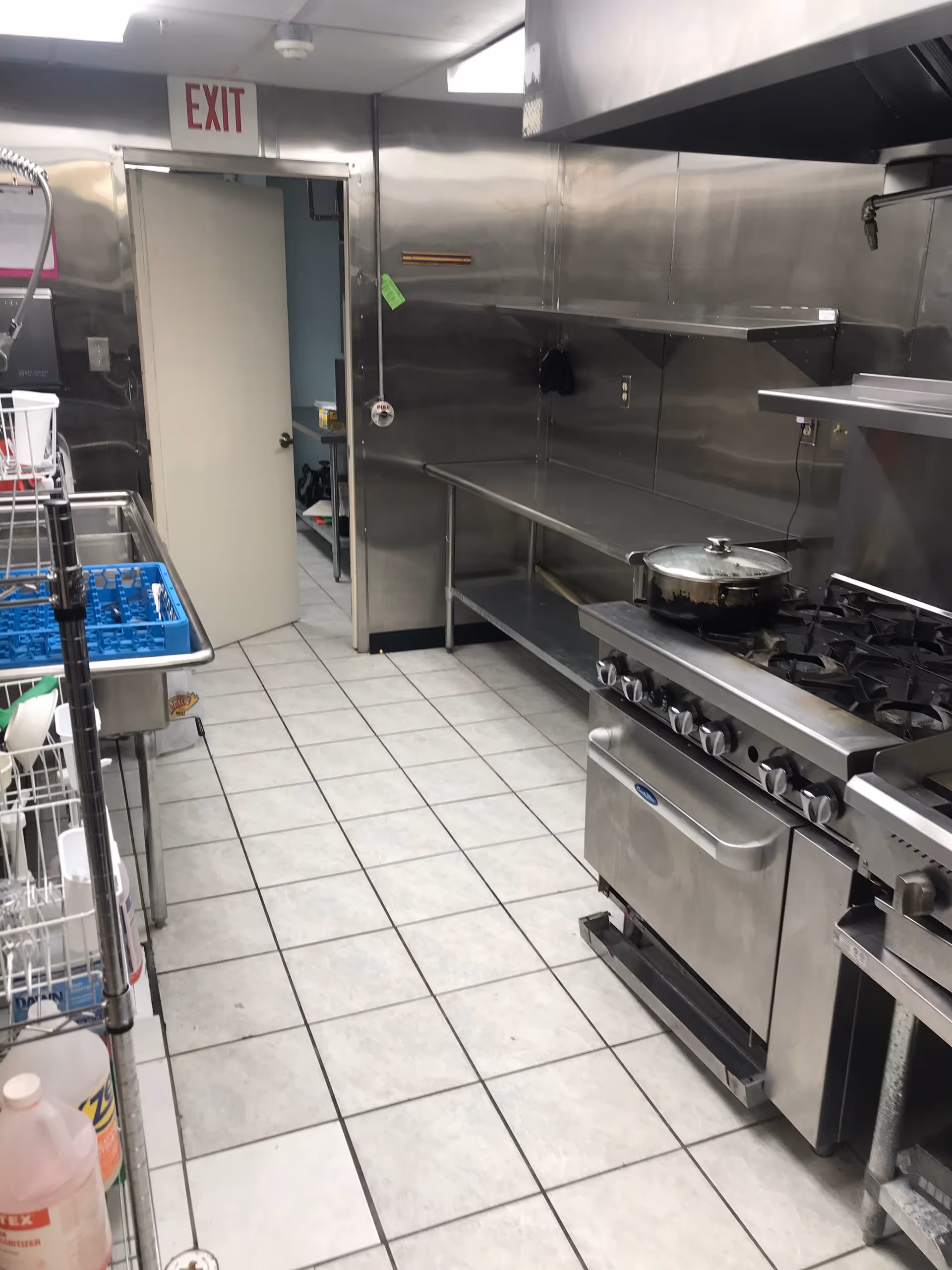 Stainless steel commercial kitchen with stove, counters, and dishwashing area.