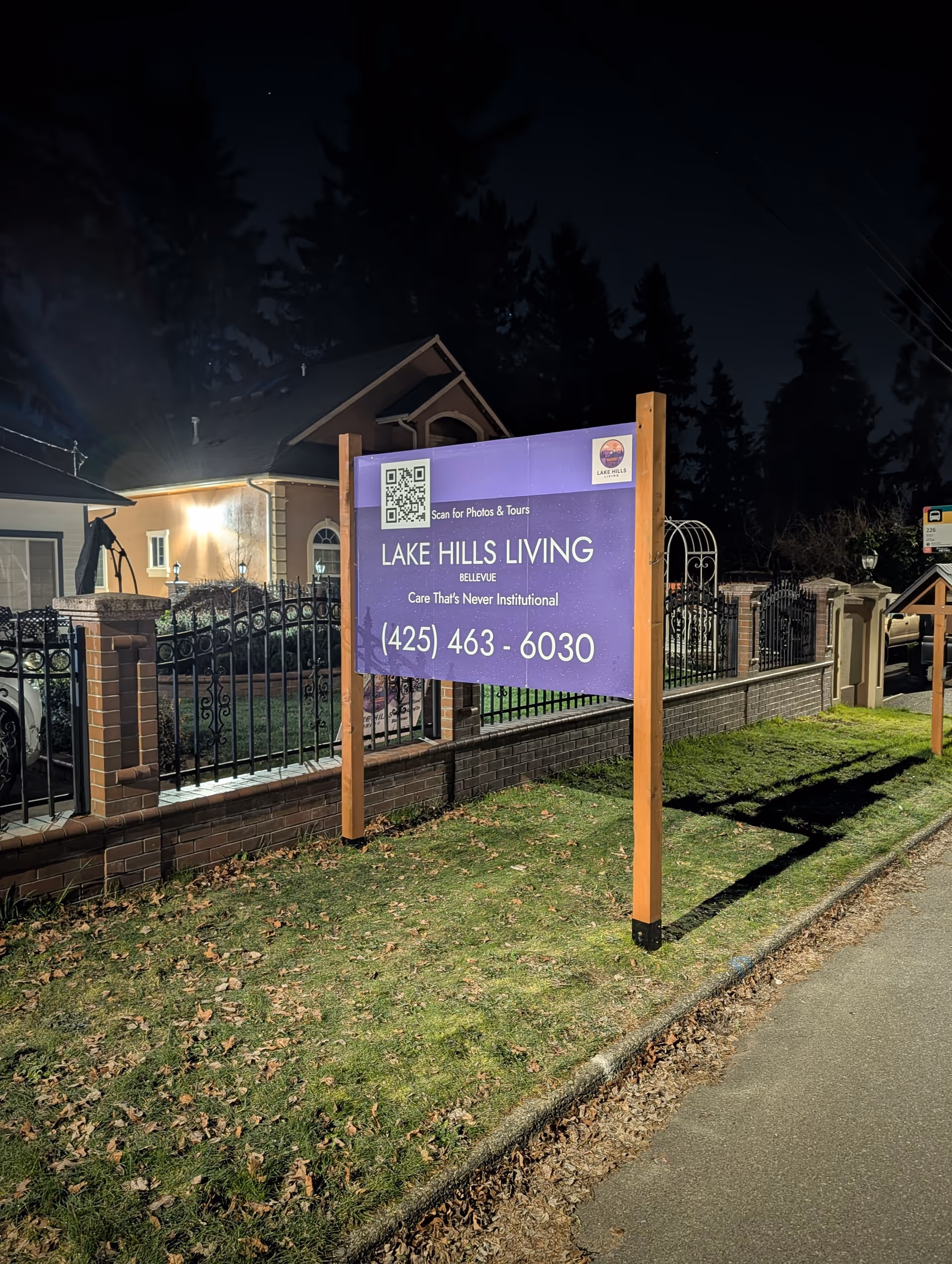 Nighttime exterior of Lake Hills Living sign with facility building and iron fence.