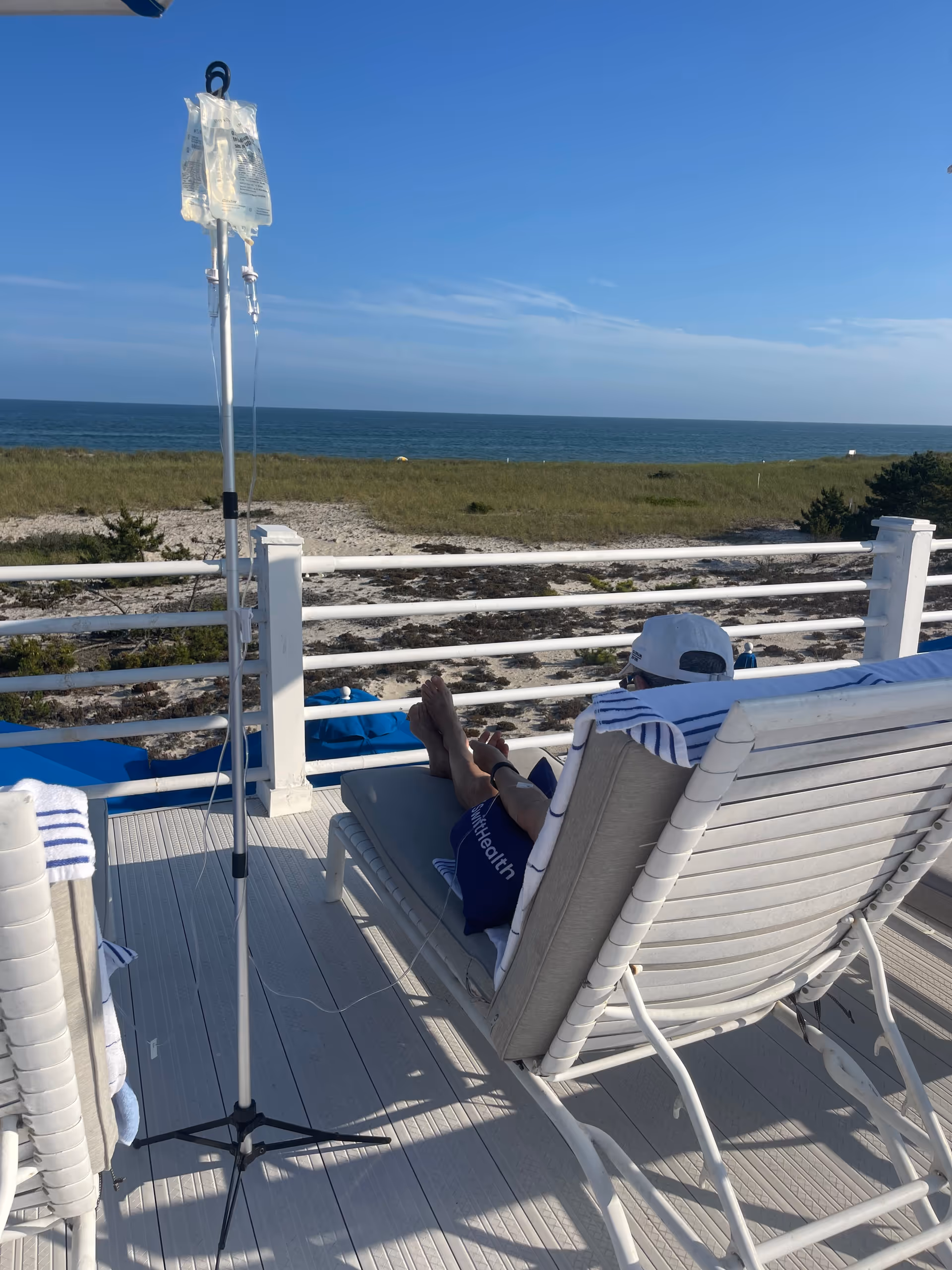 Resident reclines on a patio lounge chair overlooking the ocean with IV pole nearby.