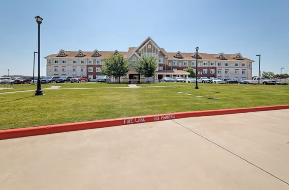 Front exterior of a large senior living facility with green lawn and parking.