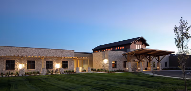Modern stone senior living building with a wooden entry canopy and landscaped front lawn.