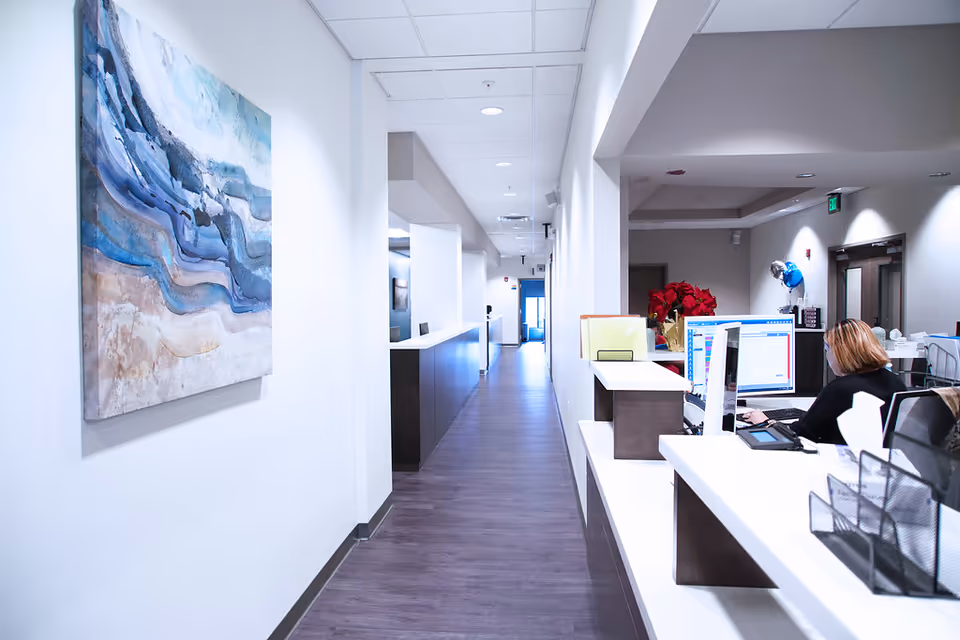 Long, well-lit clinic hallway with a reception desk and staff member at computer.