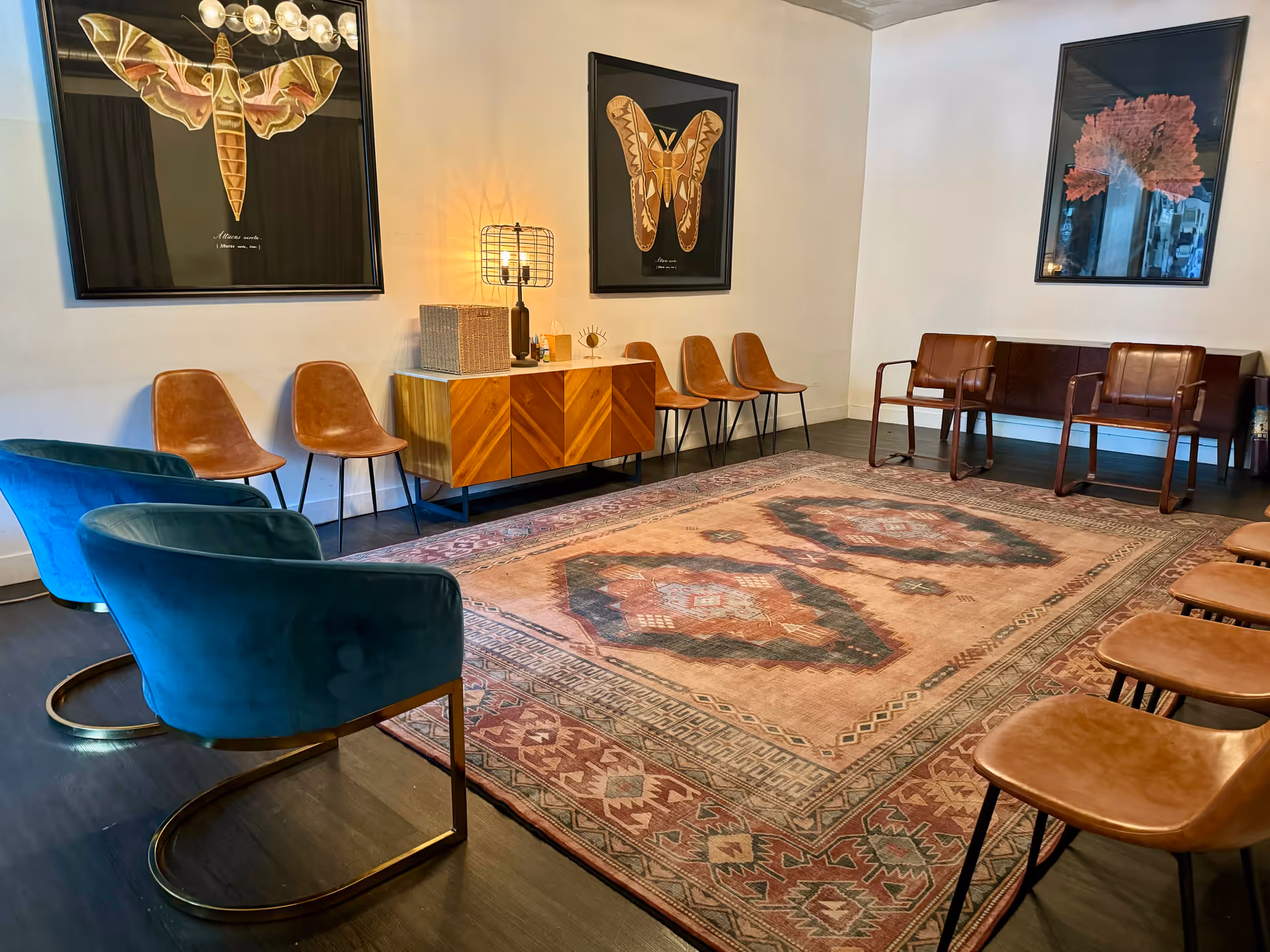 A spacious lounge area with blue accent chairs, wooden seating, and a patterned rug.