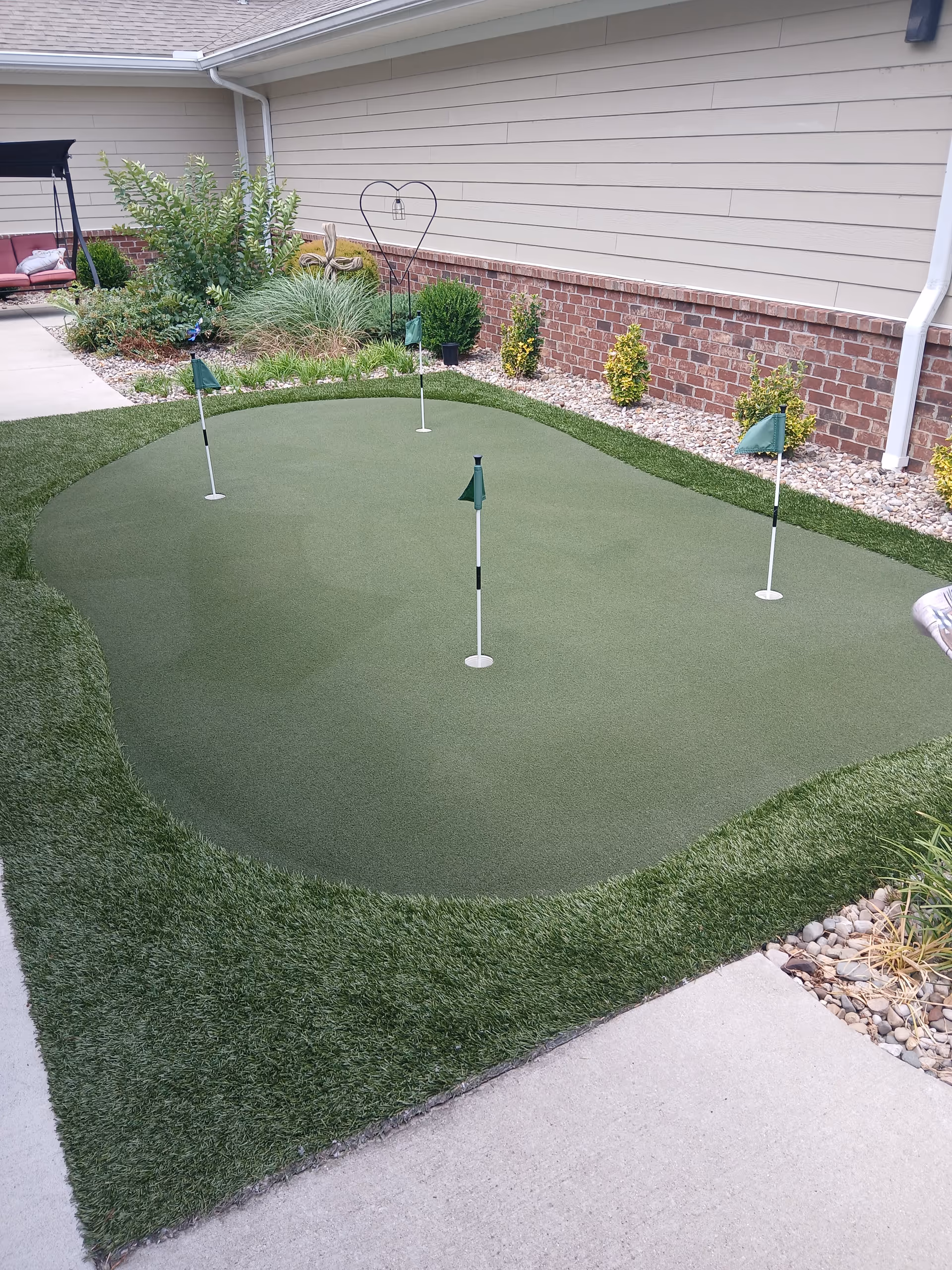 Small artificial putting green with flags in a landscaped outdoor courtyard beside a residential building
