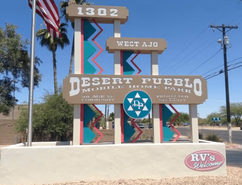Prominent decorative entrance sign for Desert Pueblo Mobile Home Park under blue sky