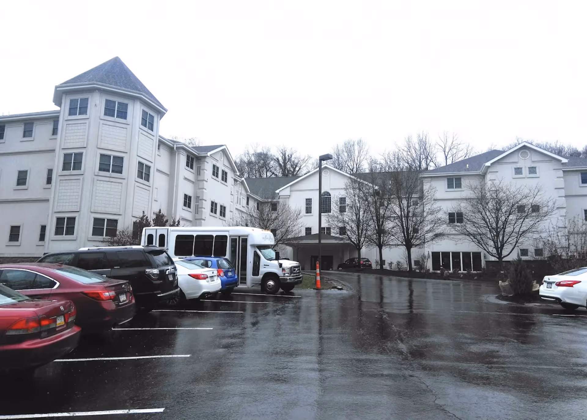 Exterior view of The Grand Residence at Upper St. Clair with parked cars and a bus.