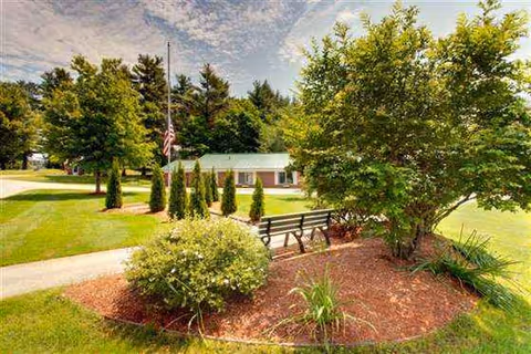 Well-kept outdoor area with walkway, bench, landscaping, flagpole, and a single-story facility in background.