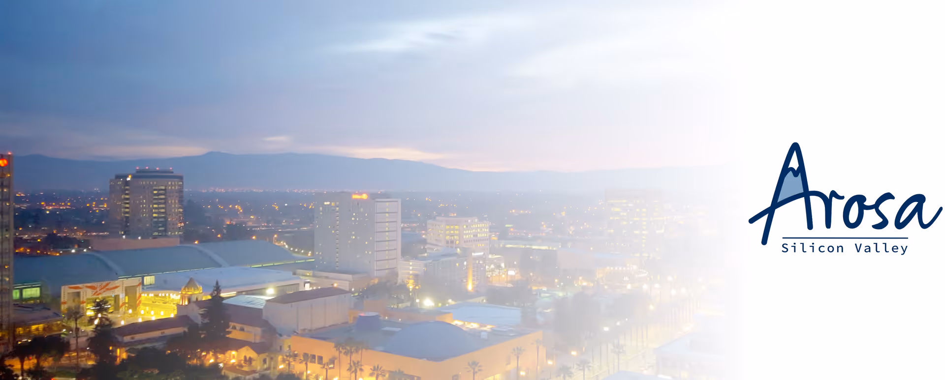 Exterior view of Arosa Silicon Valley with city skyline at dusk.