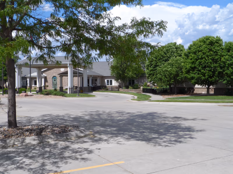Front entrance of a low-rise building with a covered drive-through canopy, landscaped trees, and an empty parking area.