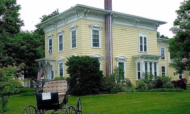 Pale yellow, two story senior home with a vintage carriage on the front lawn.