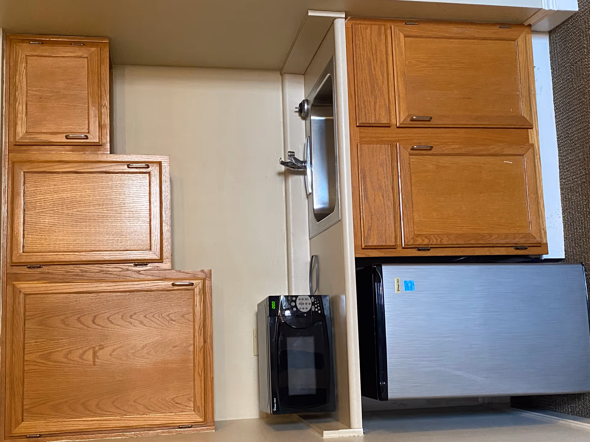 Compact kitchen in a senior living apartment with wooden cabinets, sink, microwave, and fridge.