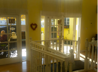 Bright yellow interior with white railings, glass doors, heart wreath, and a staircase.