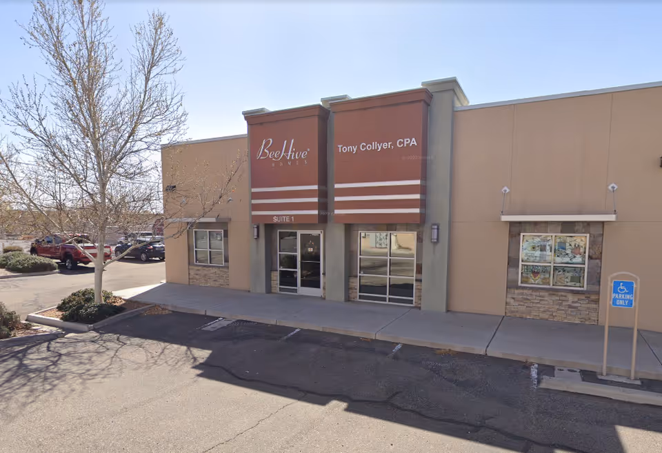 Exterior view of a beige commercial building with glass doors and red sign panels.
