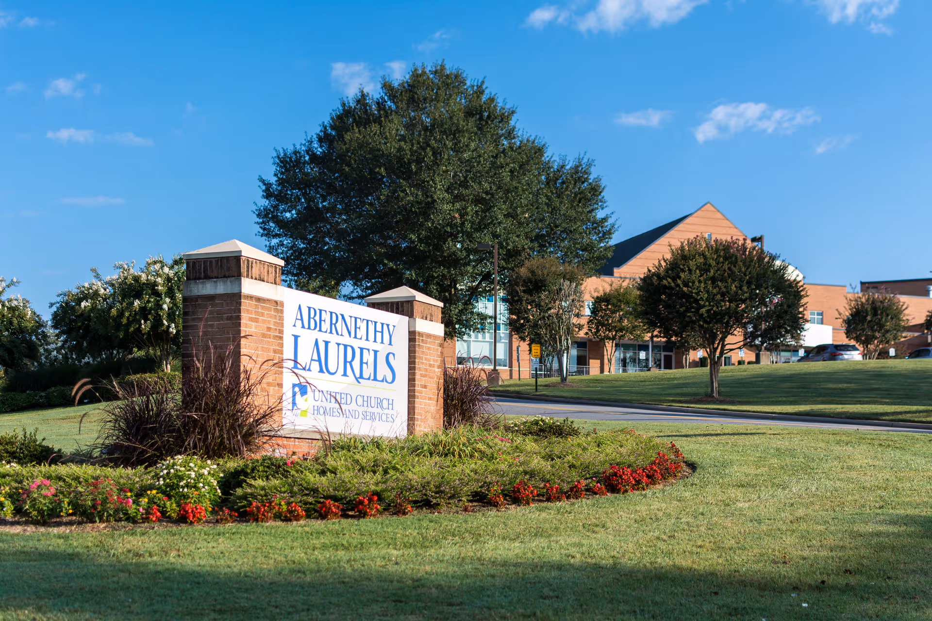 Entrance sign reading 'Abernethy Laurels' with landscaped lawns and the facility building in the background.