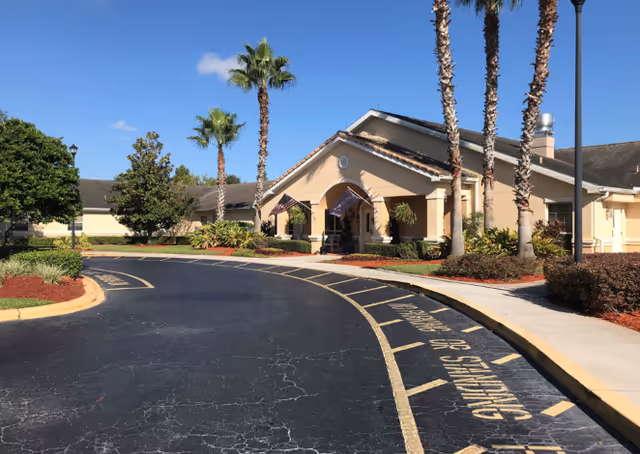 Exterior view of Arden Courts Winter Springs entrance with curved driveway and palm trees.
