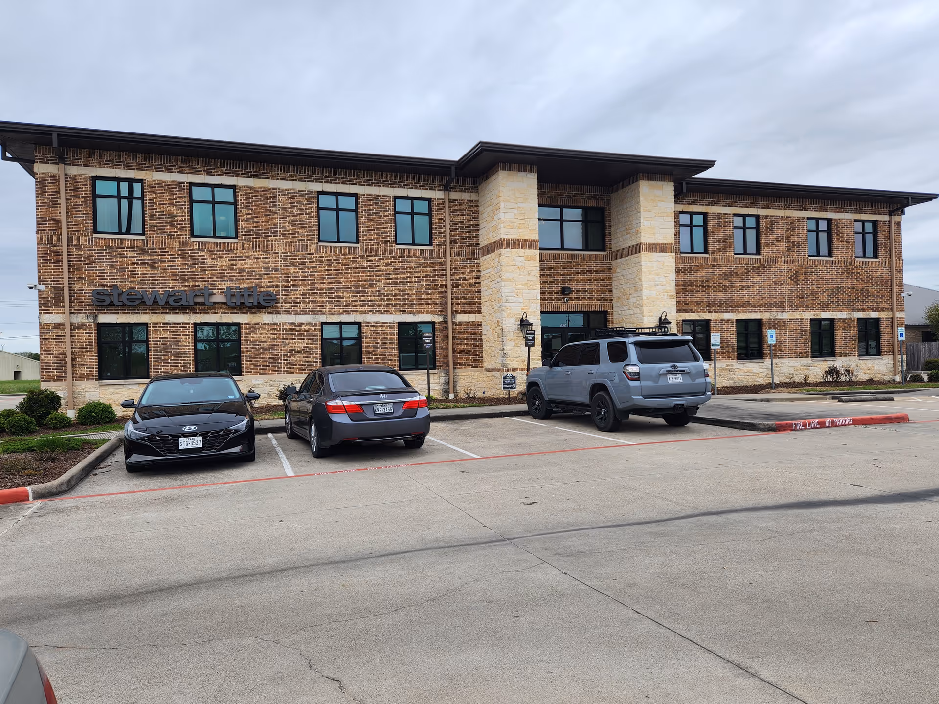 Two-story brick office building with several windows and parked cars in front.