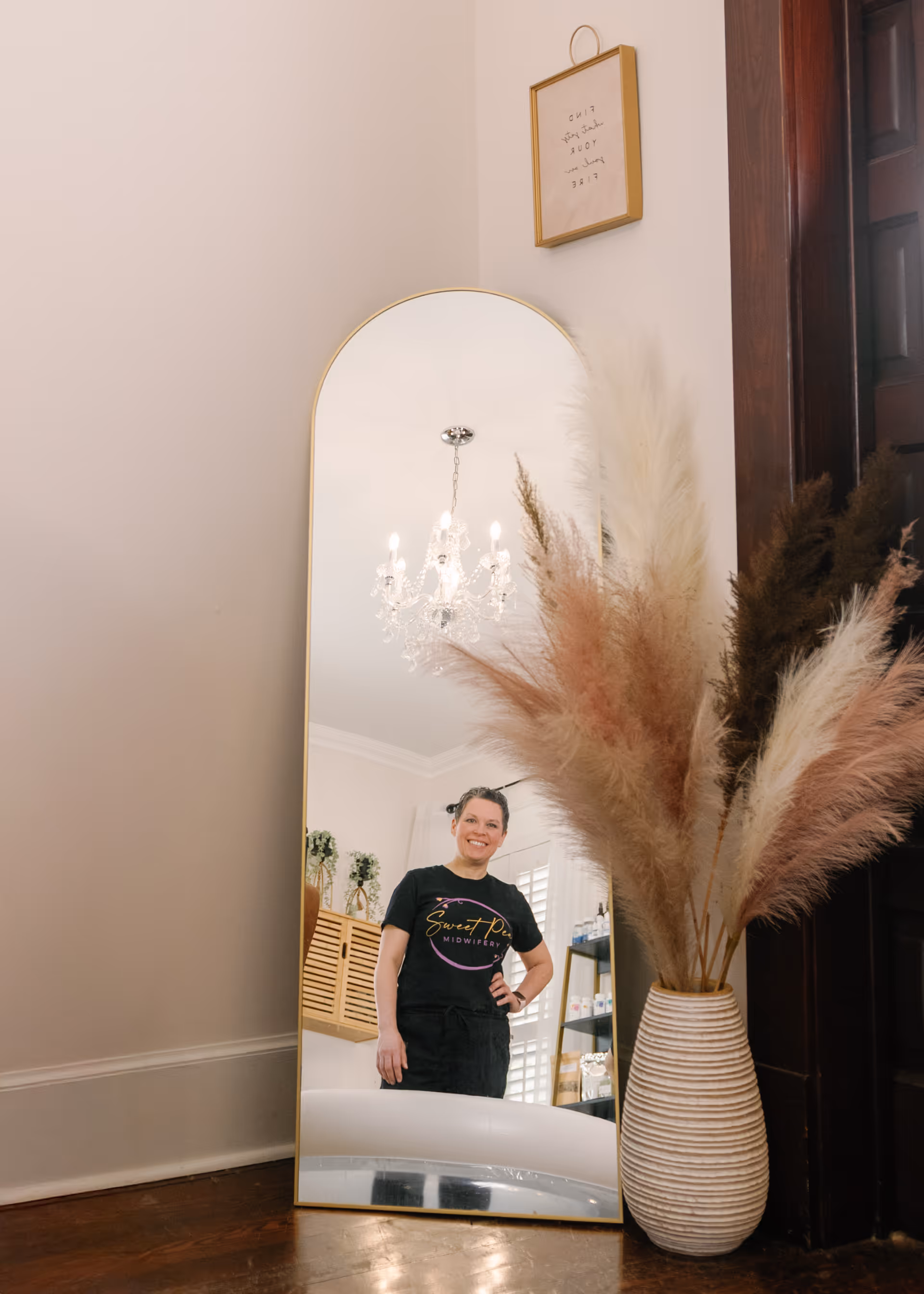 Staff member reflected in a tall mirror beside a vase of pampas grass.