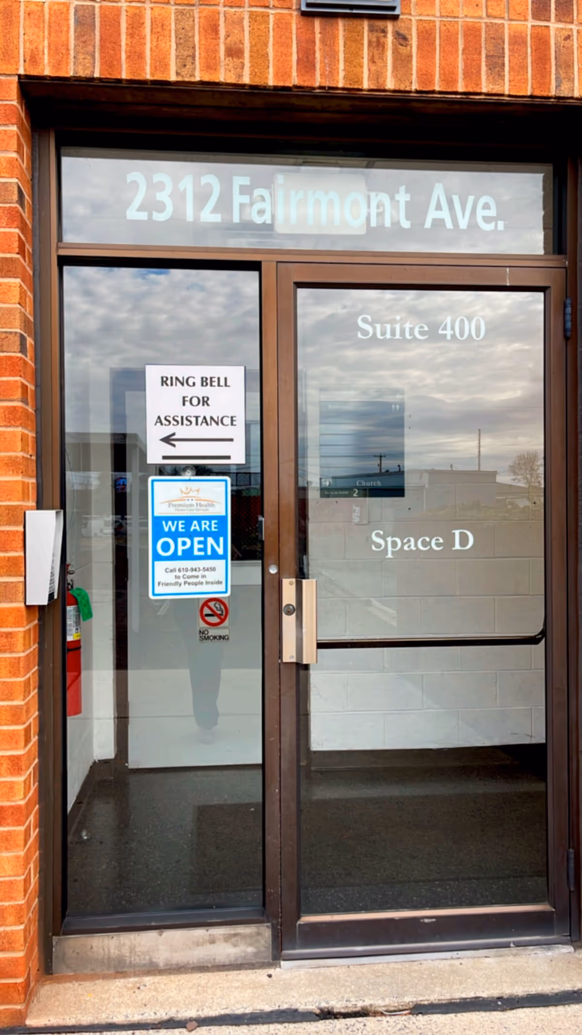 Glass storefront entrance with address, suite number, and We Are Open sign on brick exterior.