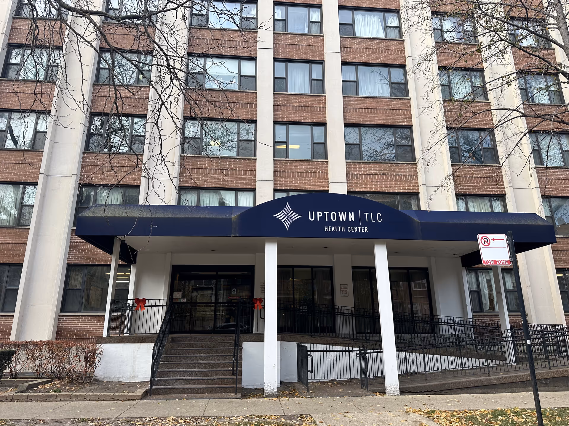Entrance of a multi-story brick health center with a navy awning reading Uptown | TLC Health Center.