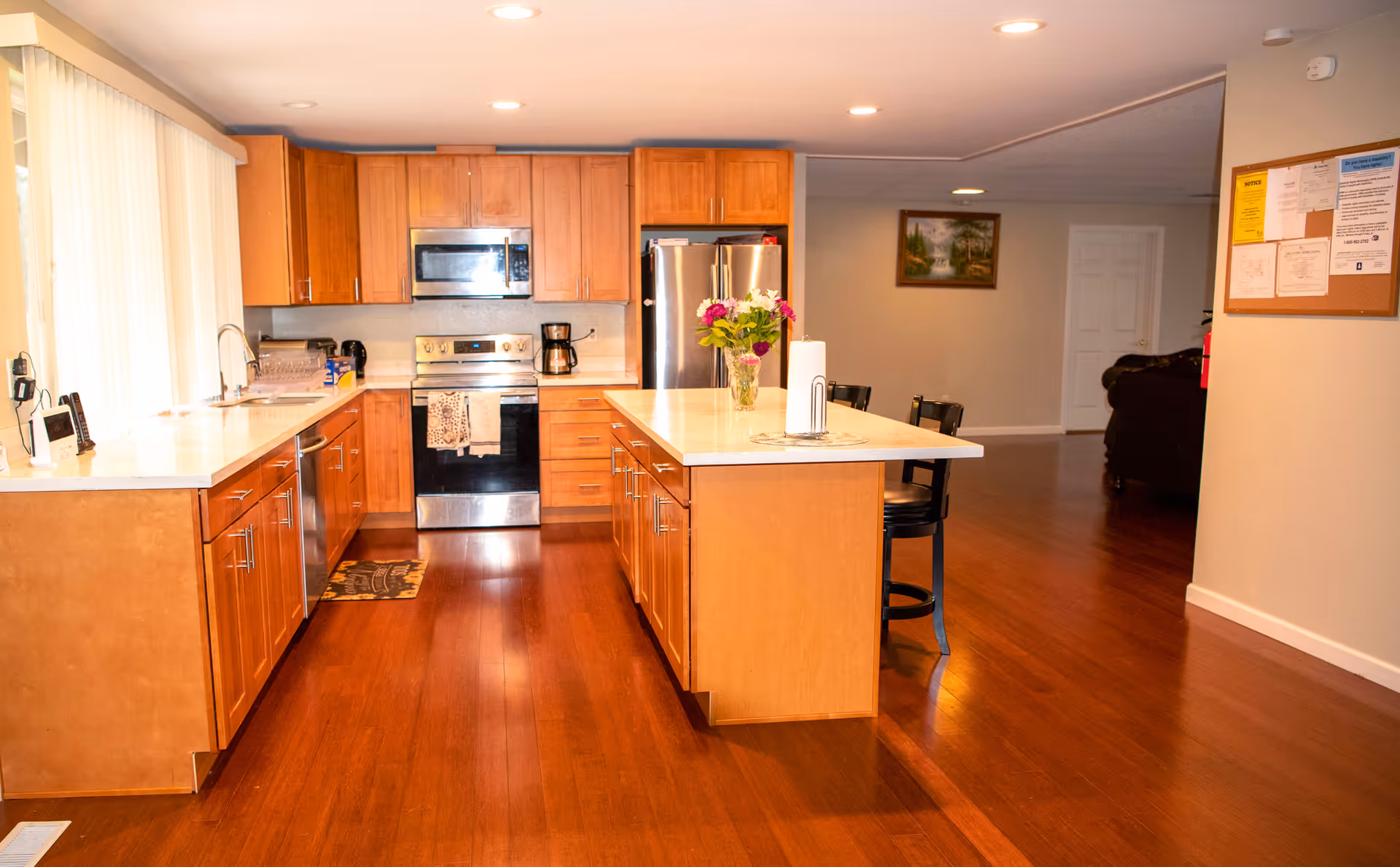 Bright open kitchen with island, wooden cabinets, stainless appliances, and stools at the island.