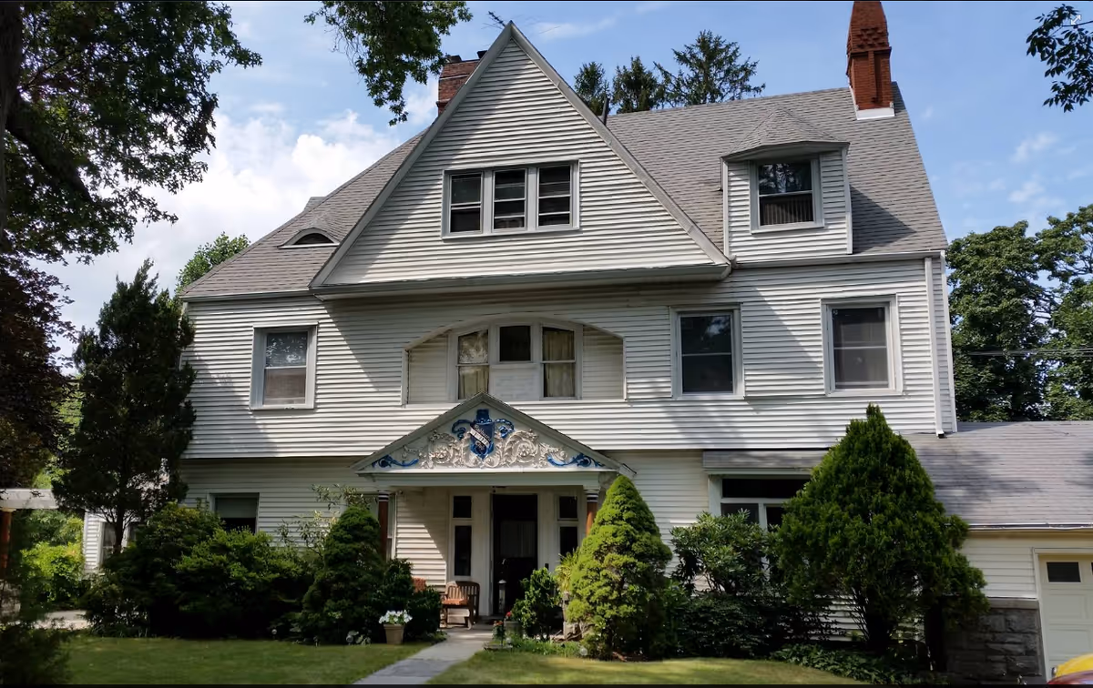 White, multi-story house-like senior living building with a front porch and lush landscaping