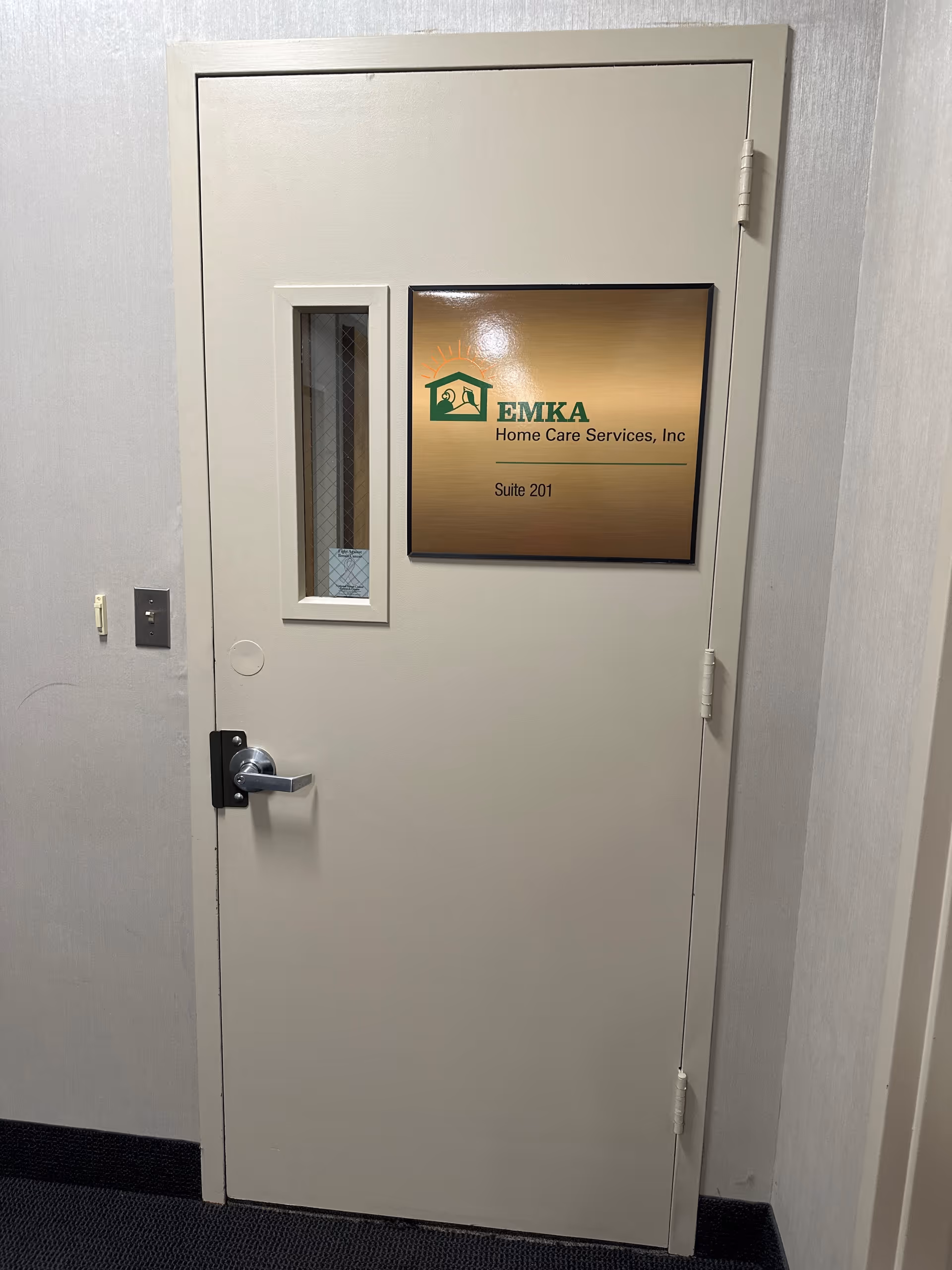 Grey interior door with window and EMKA Home Care Services Suite 201 sign