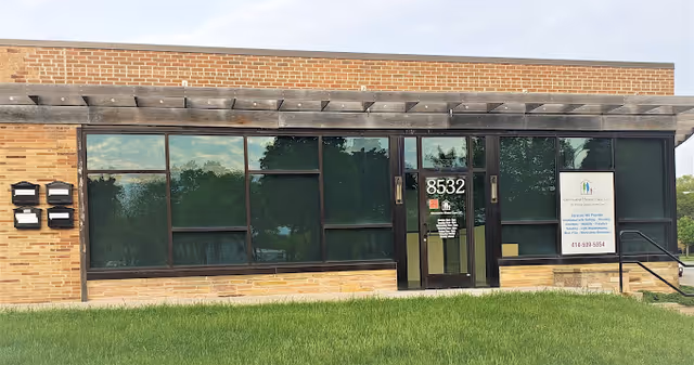 Exterior view of a single-story brick building with large windows and a sign.