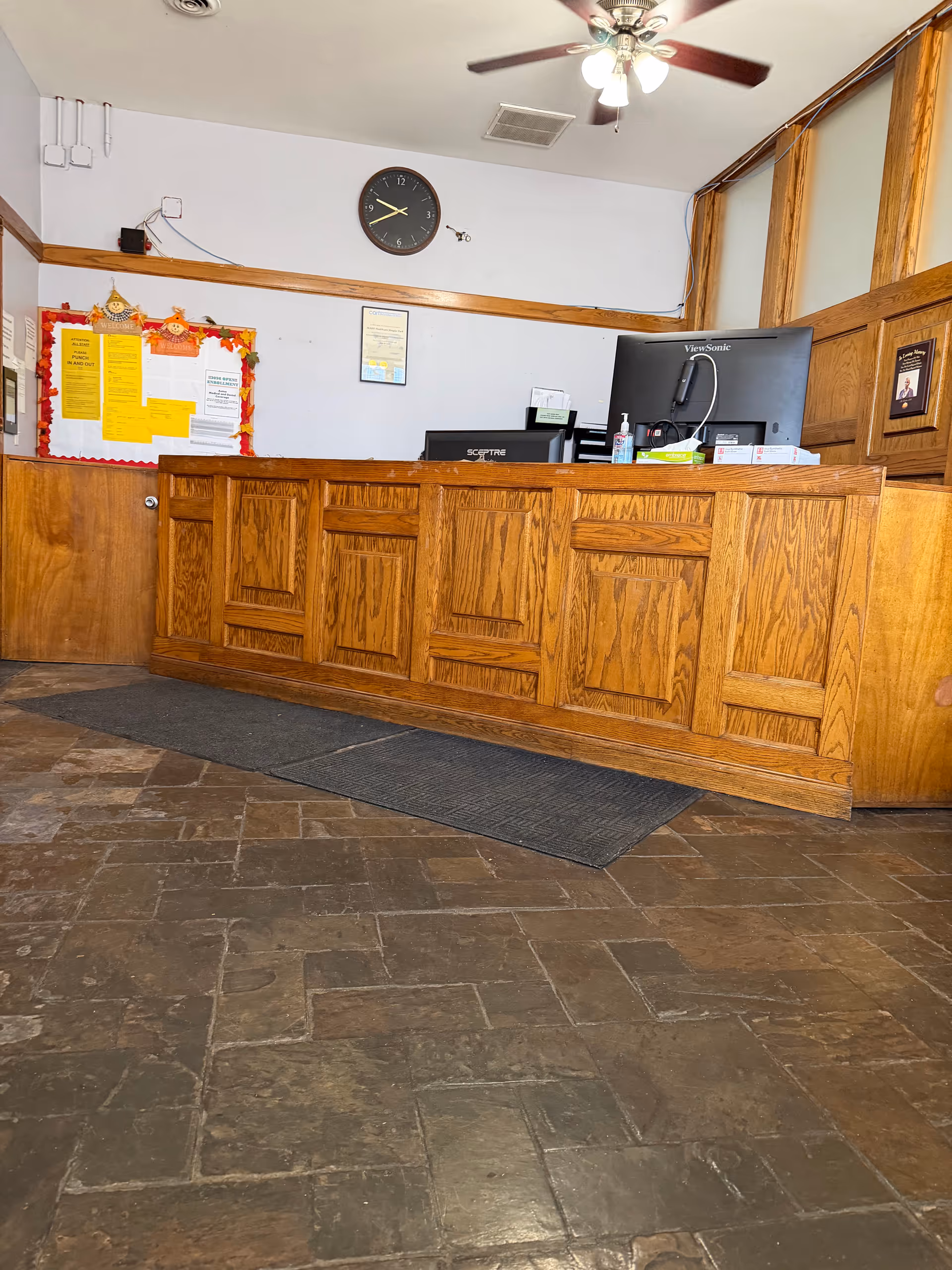 Wooden reception desk in a senior care facility lobby with a clock.