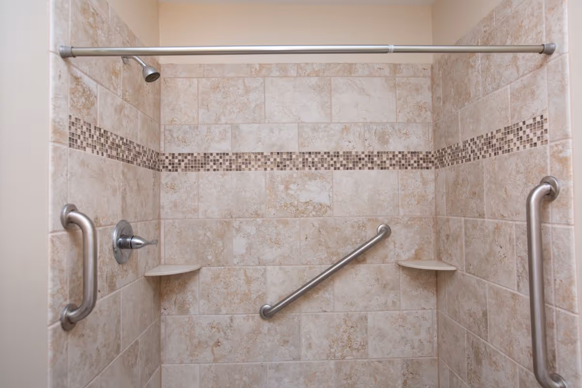 Shower stall with beige tile, grab bars, and built-in corner shelves.
