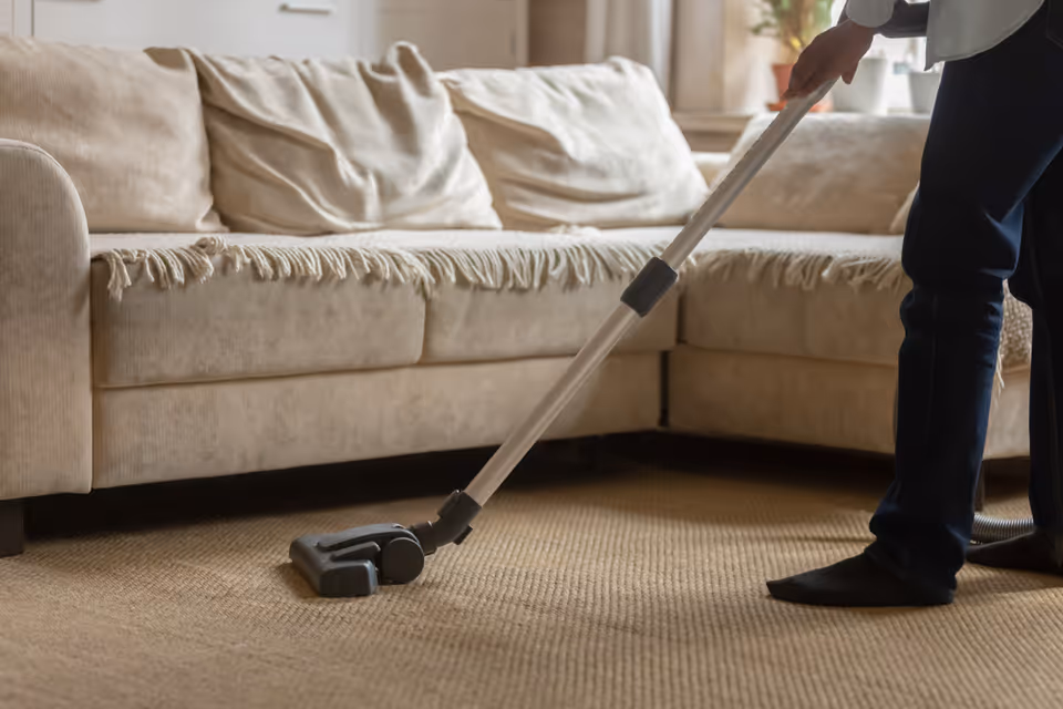 A person vacuums a beige sofa in a living room.