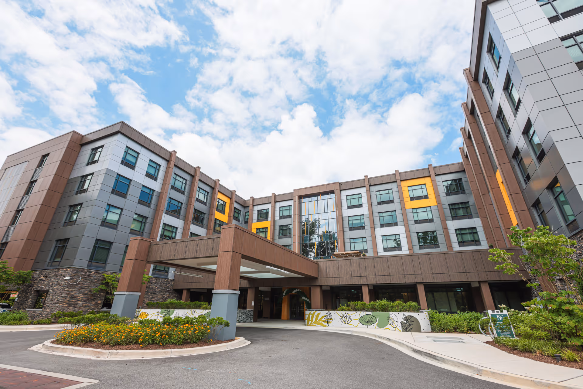 Modern, multi-story senior living building with a covered entrance and blue sky.