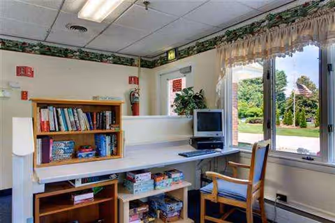 Interior desk area with computer, bookshelf, and window view in a senior facility.