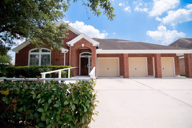 Brick-front senior living facility exterior with three garage bays and a ramp.