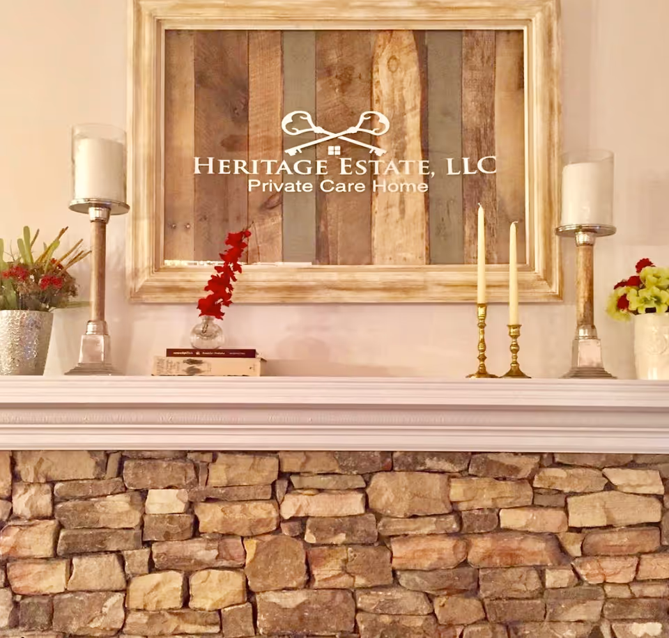 A stone fireplace mantel topped with candles, flowers and a framed wooden sign reading "Heritage Estate, LLC Private Care Home".