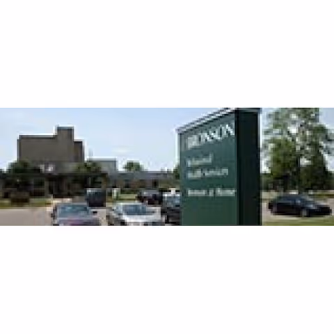 Exterior view of Bronson at Home sign with parked cars and building in the background.
