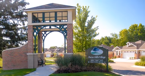 Entrance archway and sign for Porter Hills Village with nearby cottages and landscaped grounds.