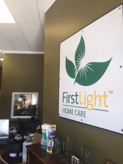 Reception area inside FirstLight Home Care with a large wall logo sign and desk.